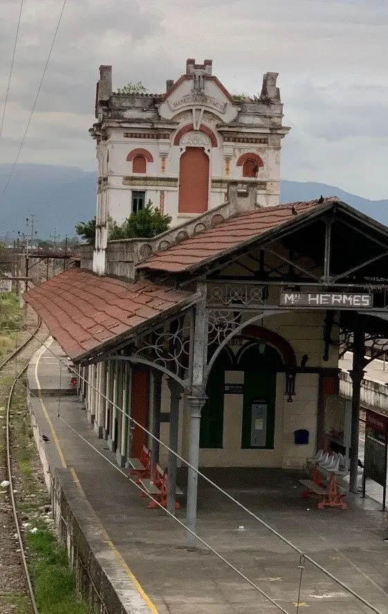 Estação ferroviária histórica com torre de pedra branca e telhado de tijolos vermelhos.
