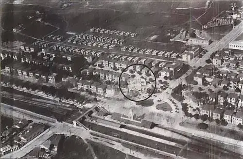 Imagem urbana em preto e branco com casas em fileira, círculo central e edifícios maiores.