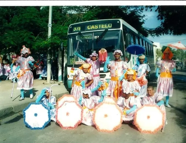 Grupo festivo com trajes coloridos e guarda-chuvas em frente a ônibus "Castelo" 378.