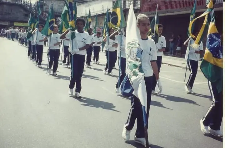 Desfile com uniformes brancos e bandeiras na cidade.