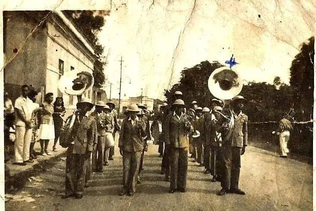 Procissão de banda antiga em preto e branco.