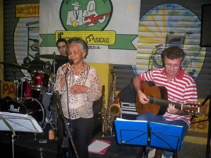 Mulher cantando em microfone, ao lado homem tocando violão, fundo com música e logotipo "30".