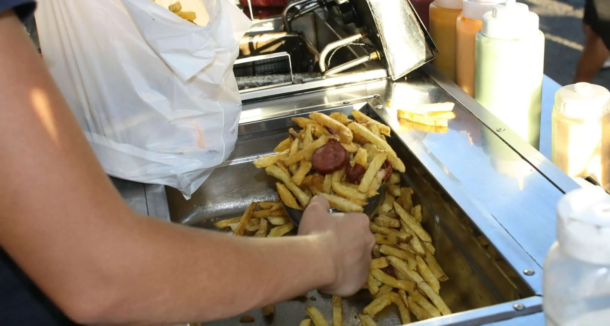 Pessoal preparando batatas fritas com salsicha em carrinho de lanches.