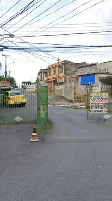 Uma rua residencial com carro amarelo, cone de trânsito e casas coloridas ao fundo.