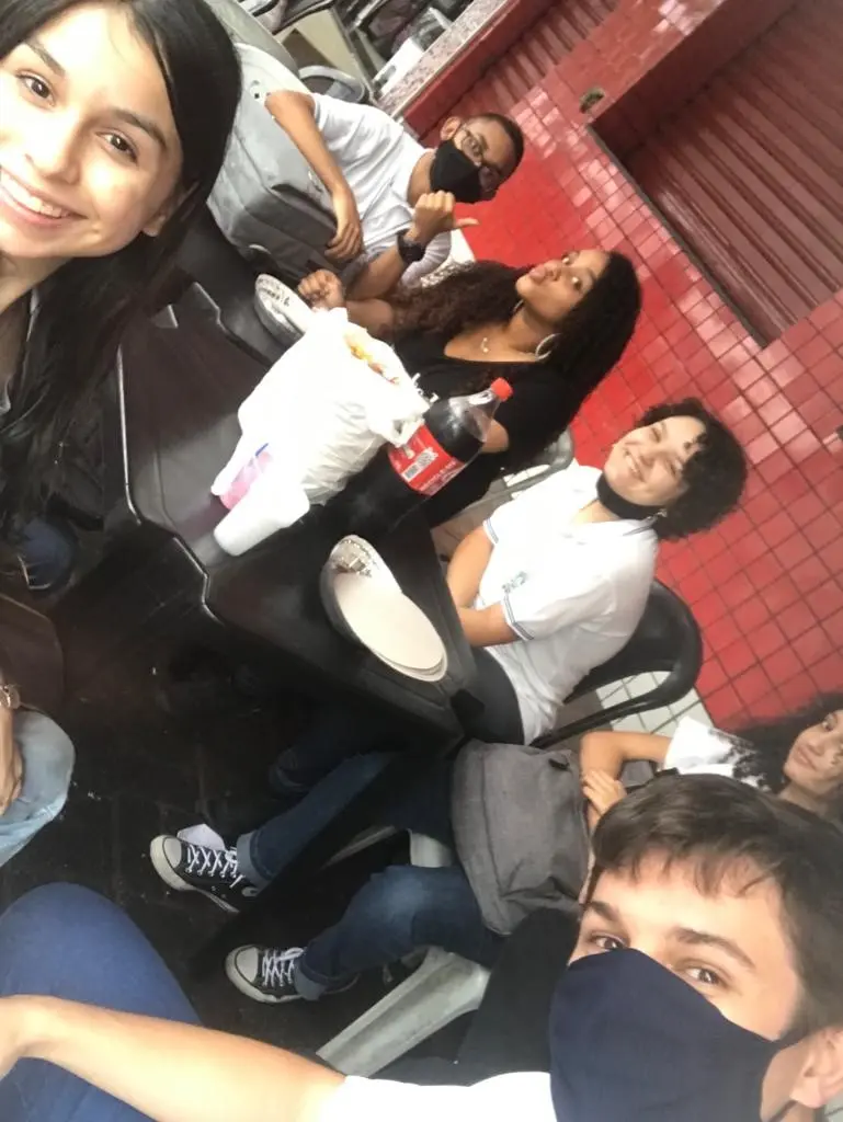 Reunião de amigos em ambiente interno, com cinco pessoas sorrindo.