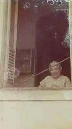 Homem sorridente em janela de prédio vermelho.