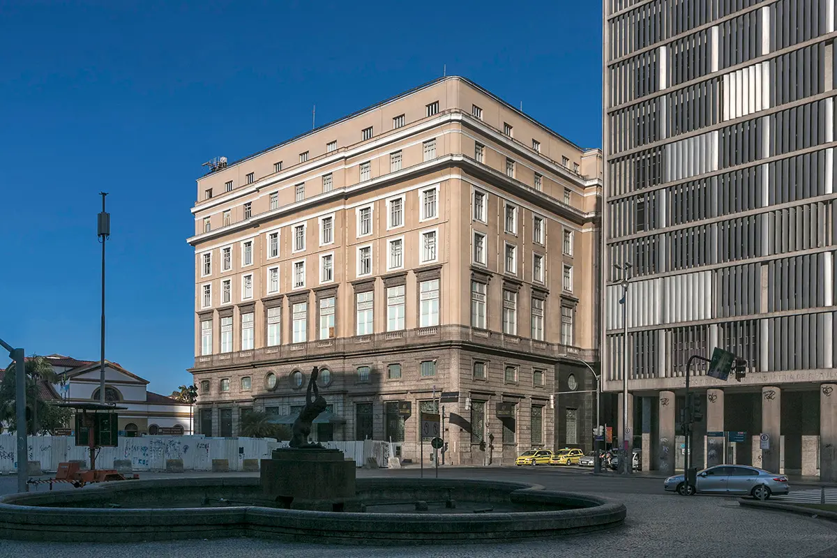 Edifício moderno em centro urbano com fonte e estátua.
