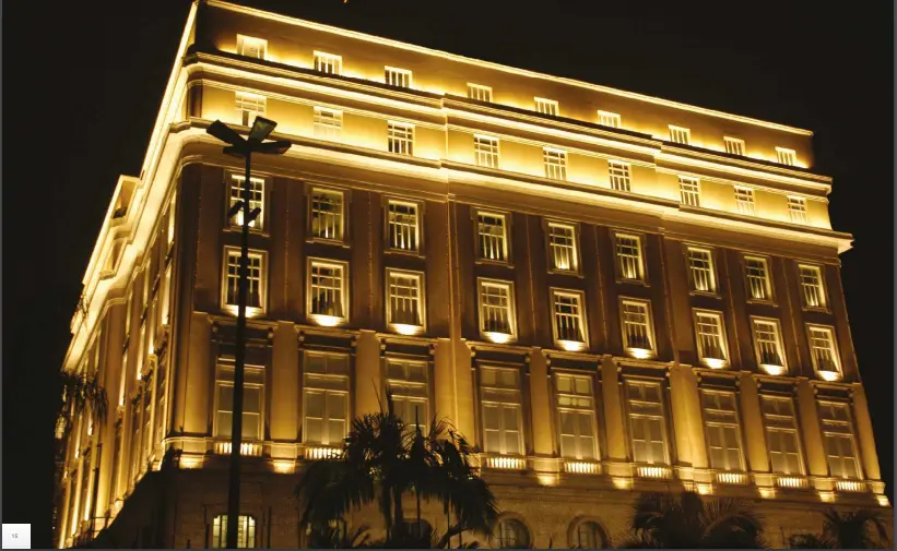 Edifício noturno com iluminação amarela e palmeira ao primeiro plano.