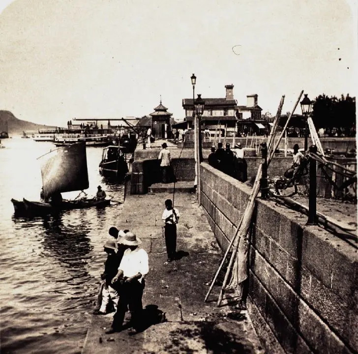 Porto antigo com embarcações e pessoas caminhando.