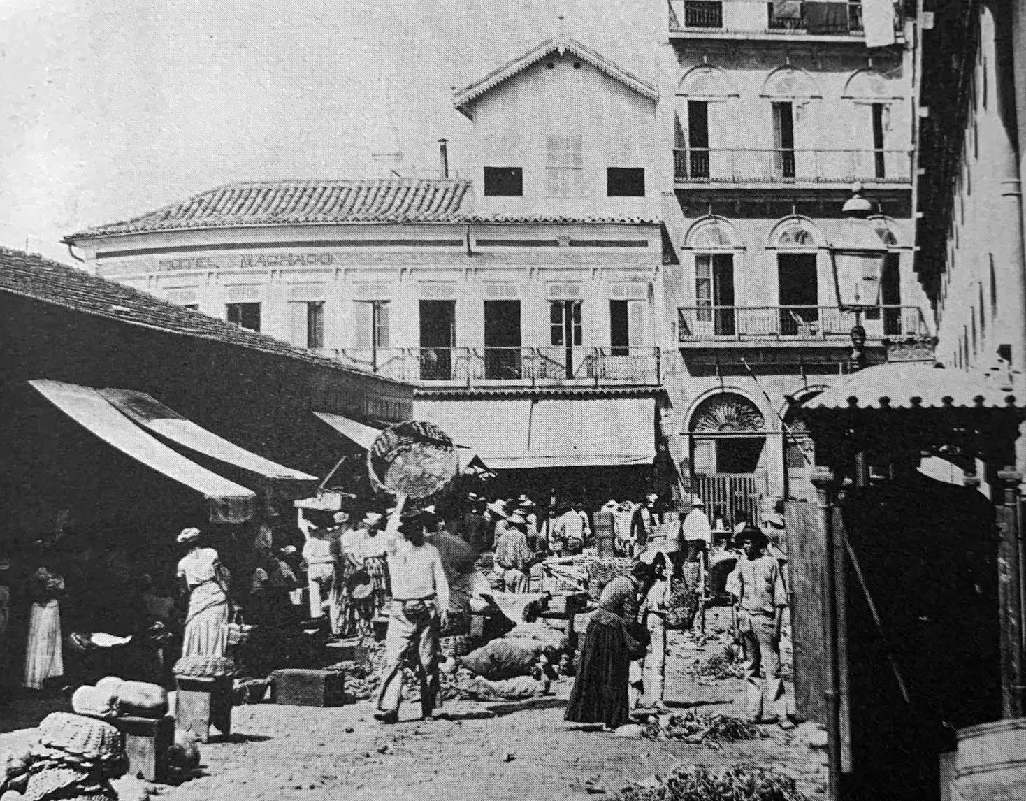 Mercado antigo com construções variadas e pessoas caminhando.