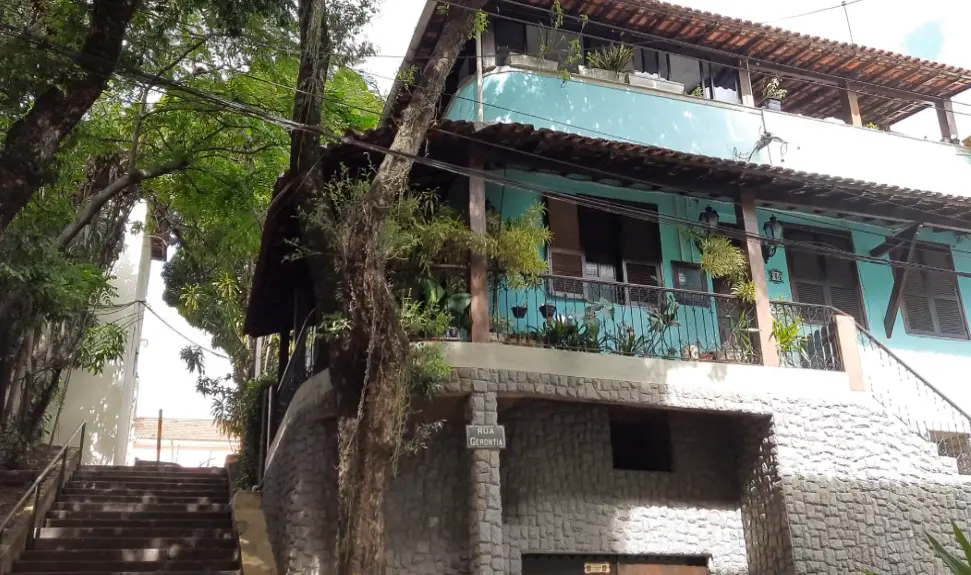 Casa azul e branca em encosta com árvores e varandas.