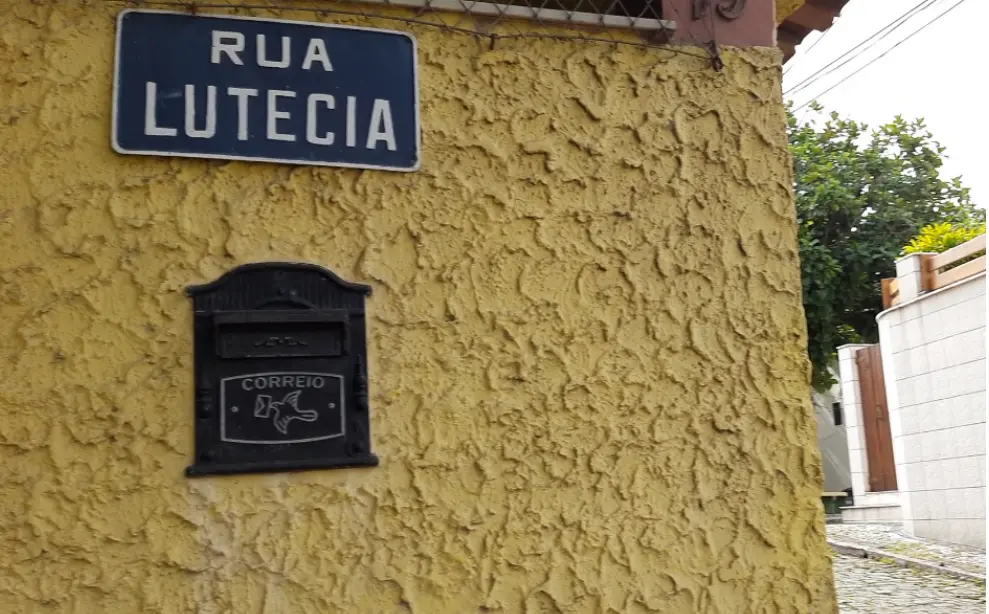 Parede amarela com sinal azul e caixa de correio preta.
