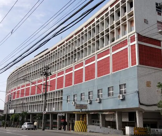 Prédio comercial com fachada colorida, placa "CADEG", entrada amarela e preta, árvore e carros na calçada.