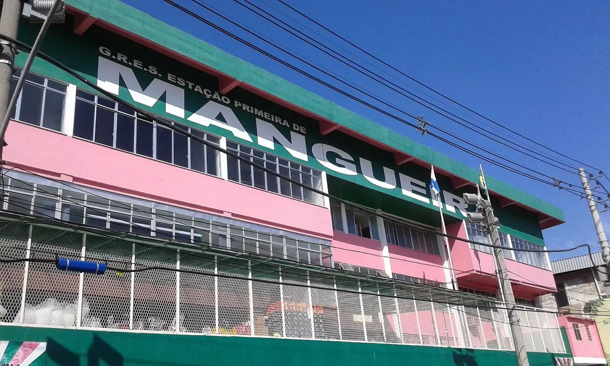 Prédio verde com detalhes rosa, grade metálica branca e sinal "G.R.E.S. ESTAÇÃO PRIMEIRA DE MANGUEIRA".