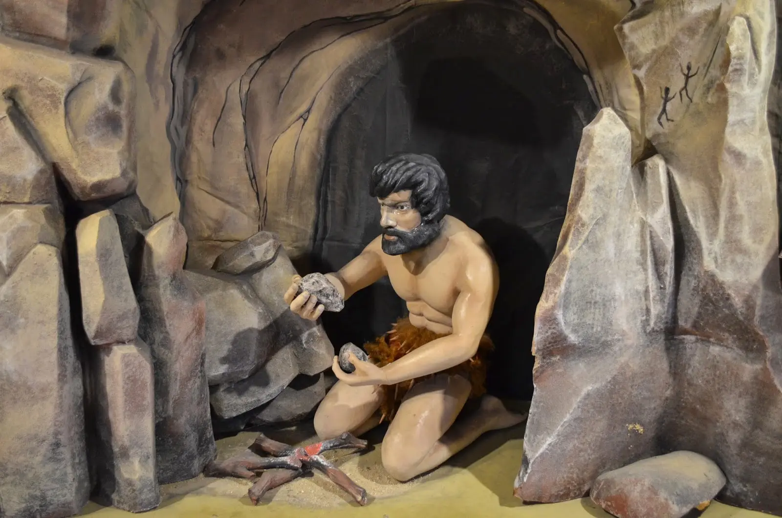 Escultura de homem pré-histórico em cenário rochoso.