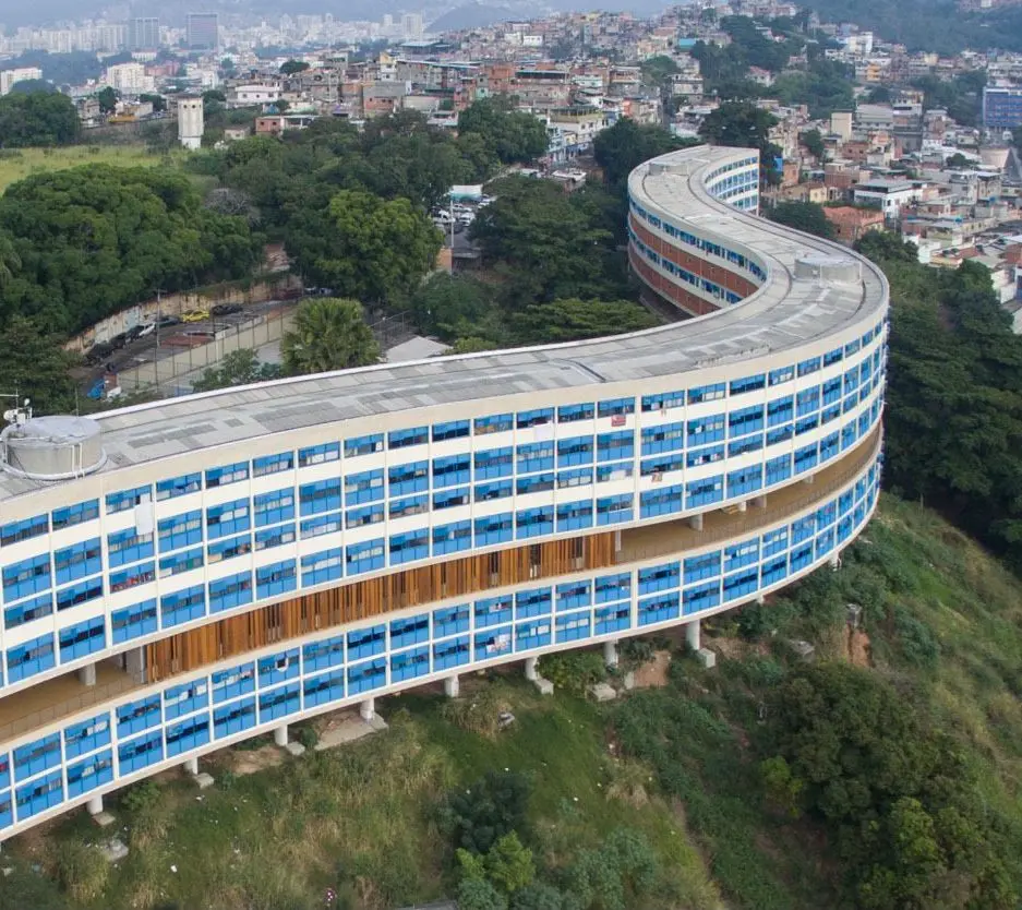 Edifício curvo em área urbana com vegetação e construções ao fundo.