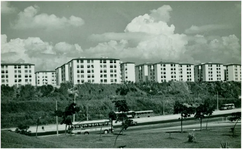 Conjunto habitacional com áreas verdes e ônibus parados.