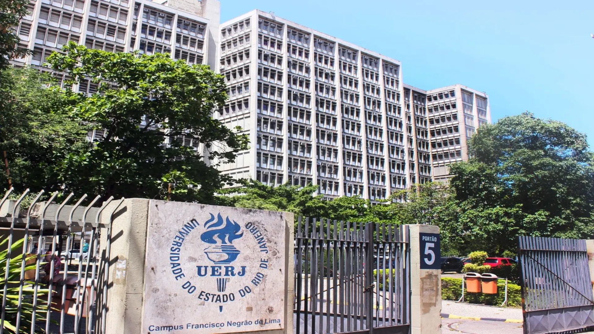 Campus universitário da UERJ com portão numerado e edifício moderno ao fundo.