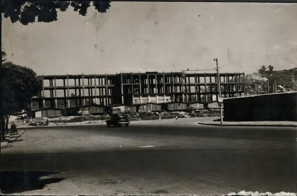 Edifício em construção com árvores e carro parado.