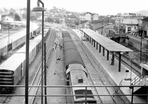 Estação ferroviária com trens parados e plataformas ocupadas.