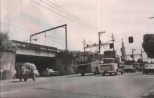 Cena urbana com túnel, motocicleta, ônibus e veículos antigos.