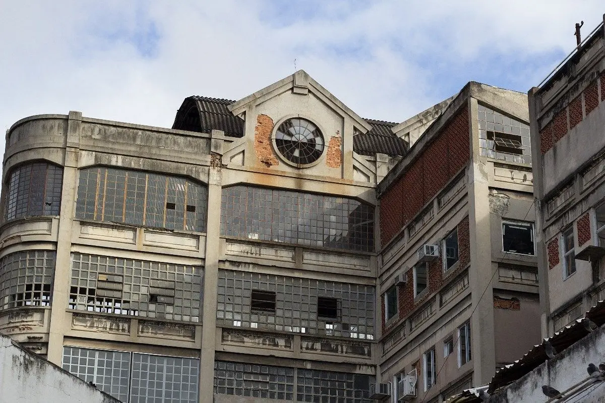 Edifício industrial antigo com fachada deteriorada e janelas quebradas.