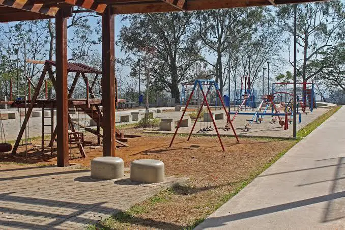 Parque com estrutura de madeira, balanços coloridos e árvores.