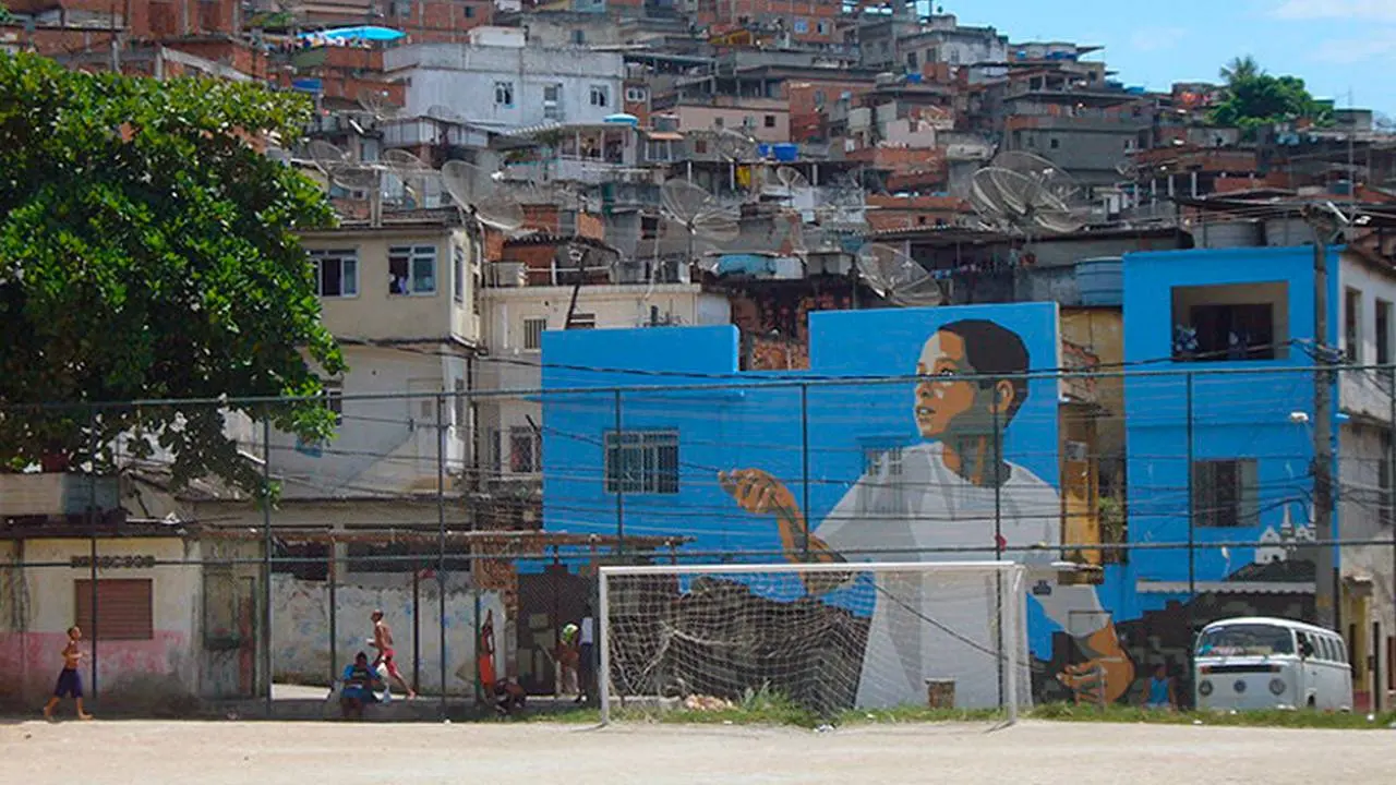 Bairro com edifícios empilhados nas encostas, muralha azul e árvore verde.