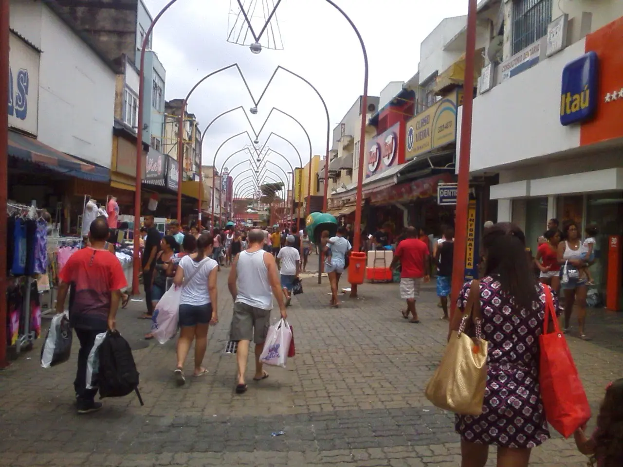 Uma rua movimentada com pessoas caminhando e lojas à esquerda.