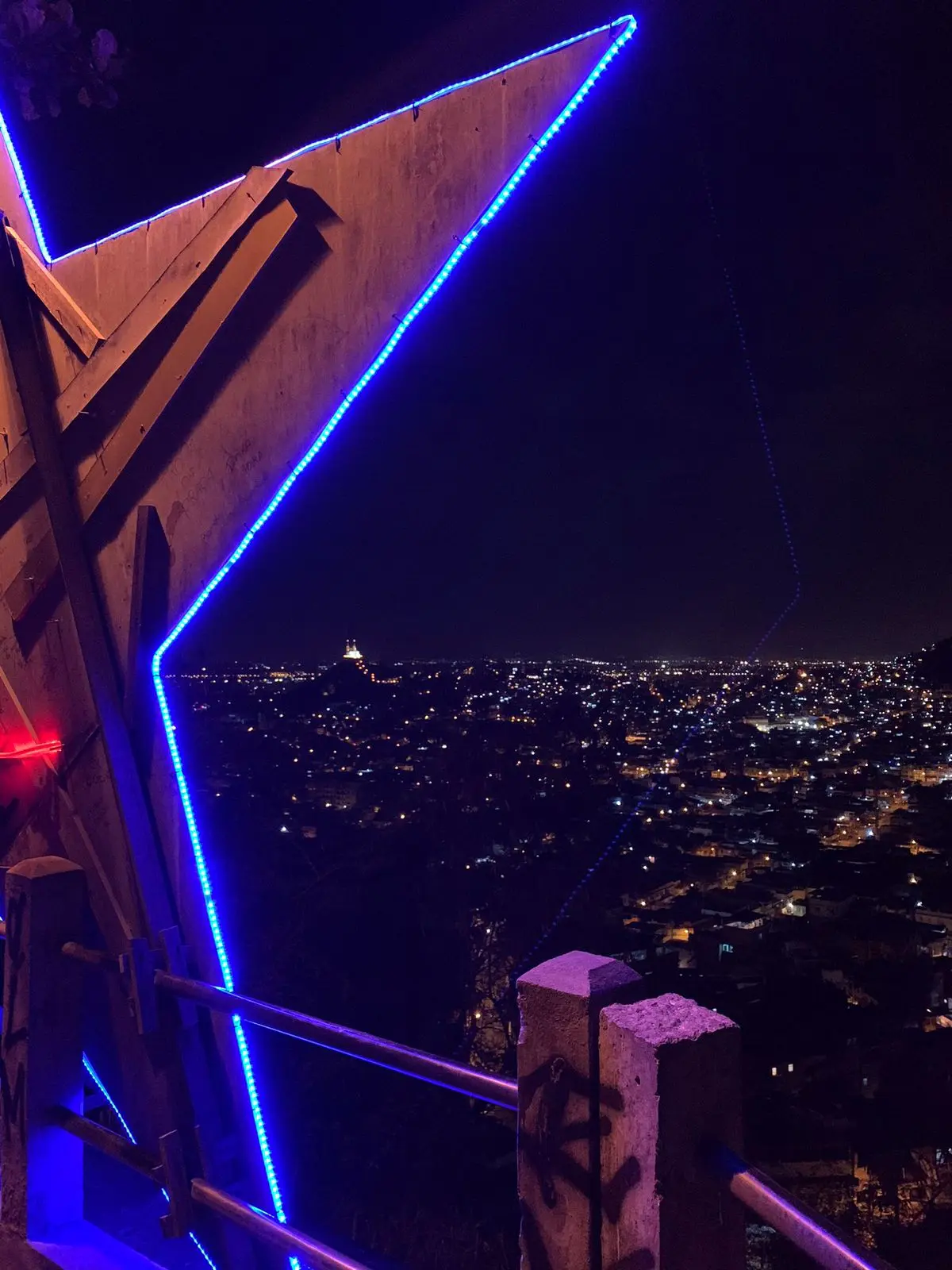 Monumento Estrela da Penha noturno com luzes azuis e cidade ao fundo.
