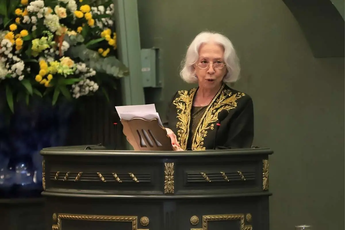 Mulher falando em púlpito com flores amarelas e brancas ao lado.