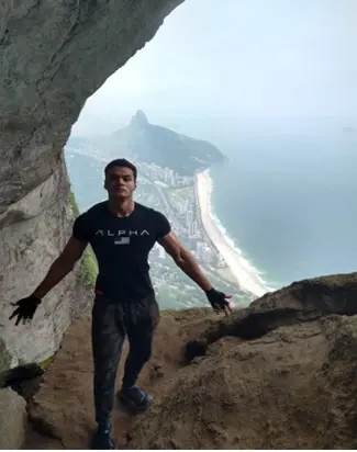 Homem em equilíbrio em caverna rochosa, mar ao fundo.