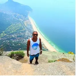 Pessoas em pé em local elevado, praia e cidade ao fundo.