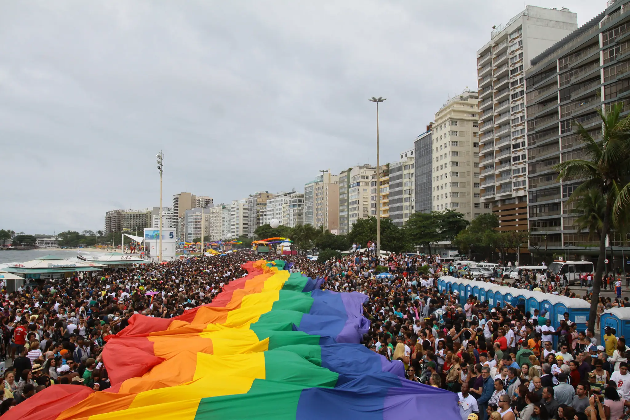 Parada LGBTQIAP+ com multidão colorida e bandeira arco-íris.