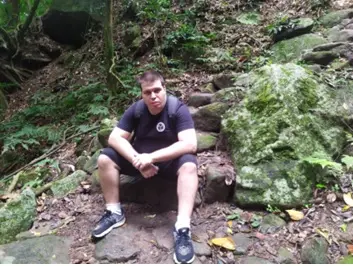 Homem sentado em rocha na floresta, olhando para frente.