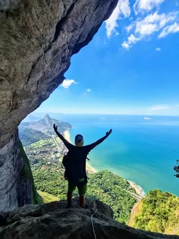 Pessoas escalando em rota montanhosa com vista para o mar.