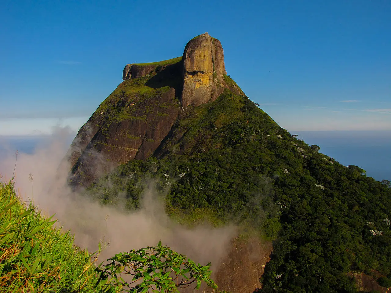 Montanha verde com vegetação densa e céu azul claro.
