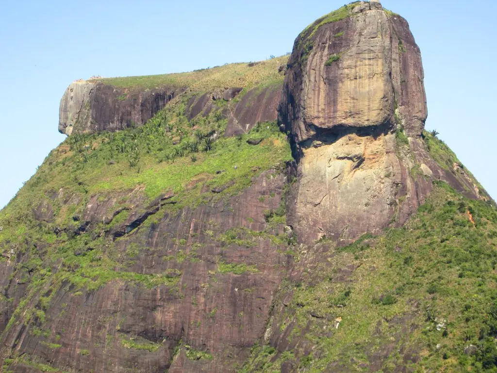 Montanha com forma irregular, vegetação verde e formação rochosa vertical.