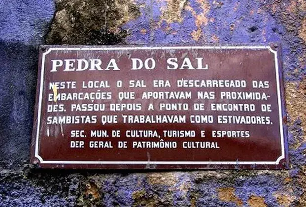 Placa informativa sobre a Pedra do Sal em parede de pedra azul.