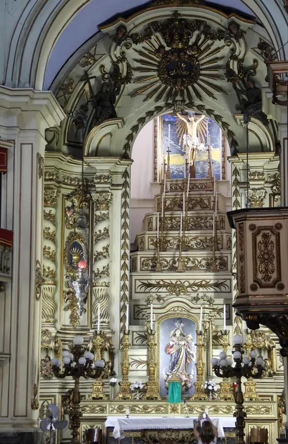 Altar ornamental em dourado e branco, com figura religiosa centralizada.