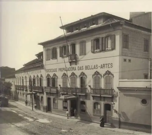Edifício histórico com fachada branca e varandas, localizado em uma rua tranquila.