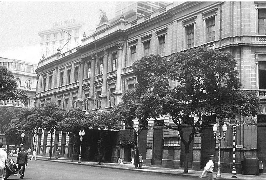 Edifício histórico em rua urbana com árvores e construções ao redor.