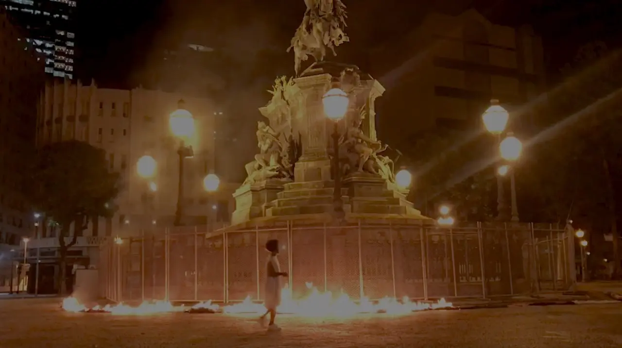 Monumento noturno em praça urbana com chamas de fogo.