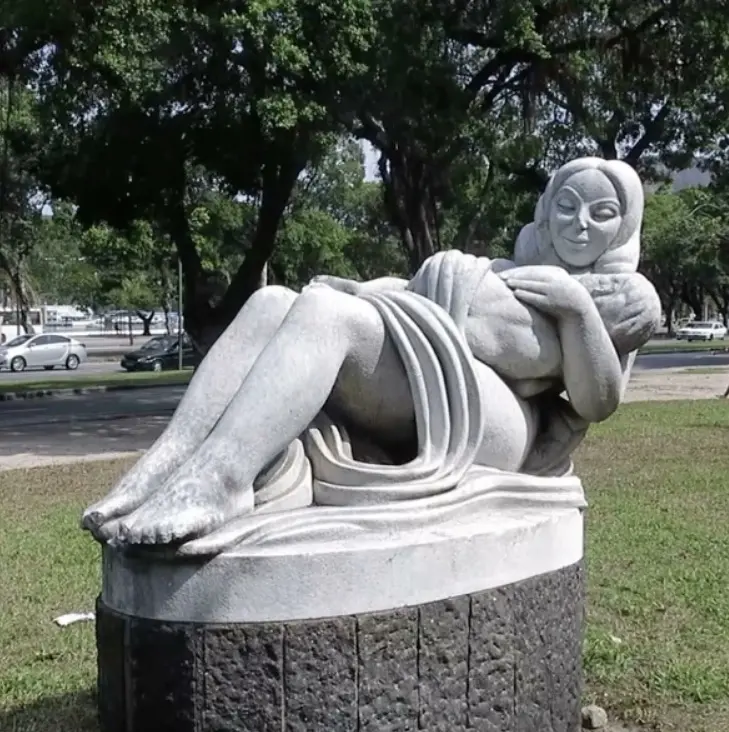 Estátua feminina deitada em pedestal em parque.
