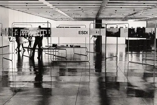 Interior moderno com pessoas caminhando e estruturas metálicas.