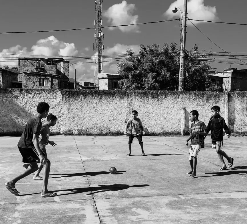 Crianças jogando futebol em pátio, céu parcialmente nublado.