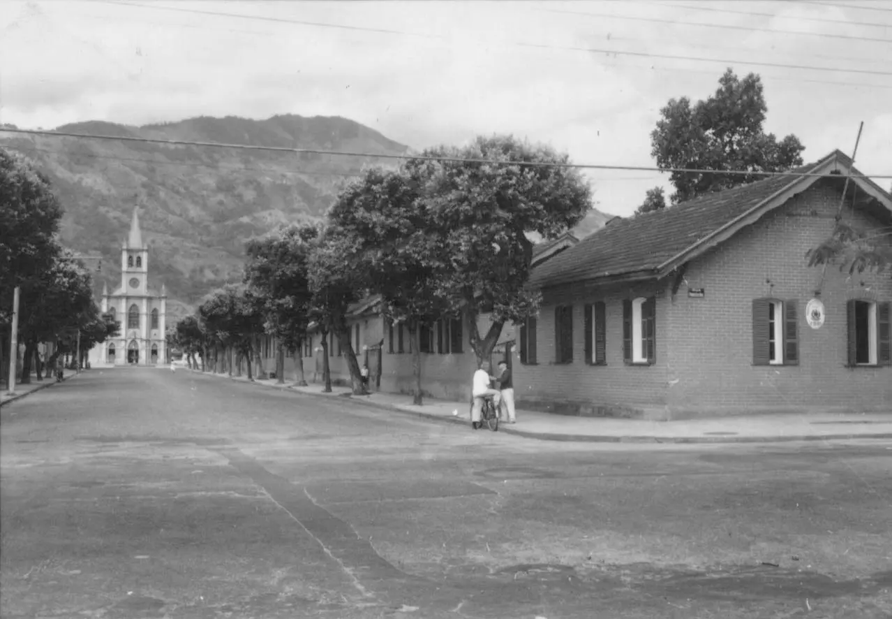 Rua com casas laterais e igreja ao fundo.