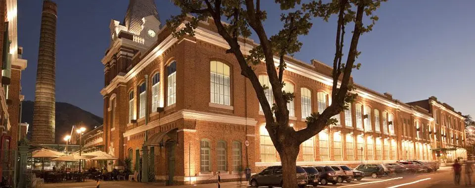 Fábrica histórica à noite com torre de fumaça e edifícios iluminados.