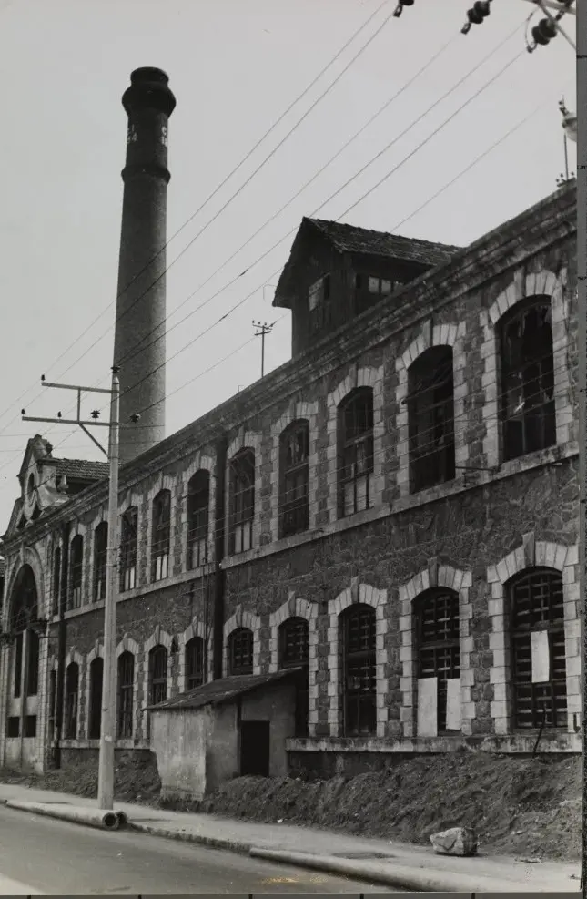 Edifício industrial com torre de fumacê e construções laterais.