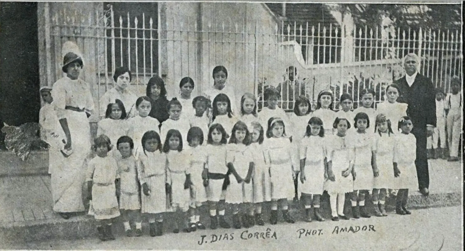 Turma escolar em foto antiga, crianças e adultos em uniformes.